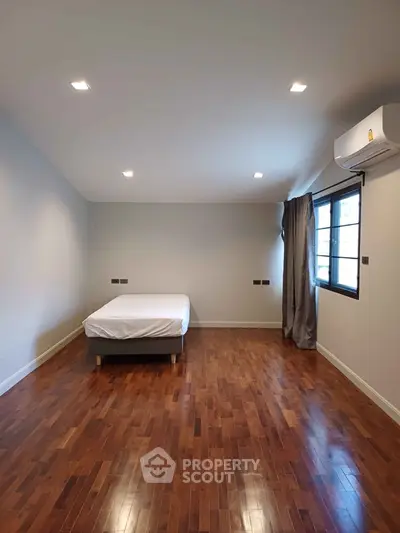 Spacious bedroom with wooden flooring and natural light