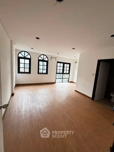Spacious living room with wooden flooring and large windows offering ample natural light.