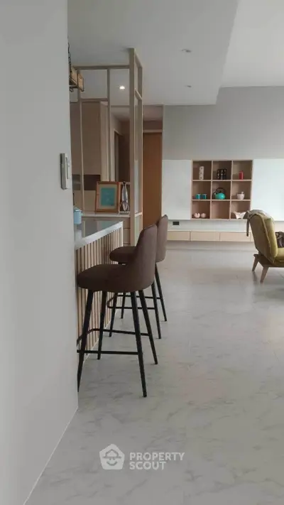 Modern open-plan living room with stylish bar stools and elegant shelving unit.
