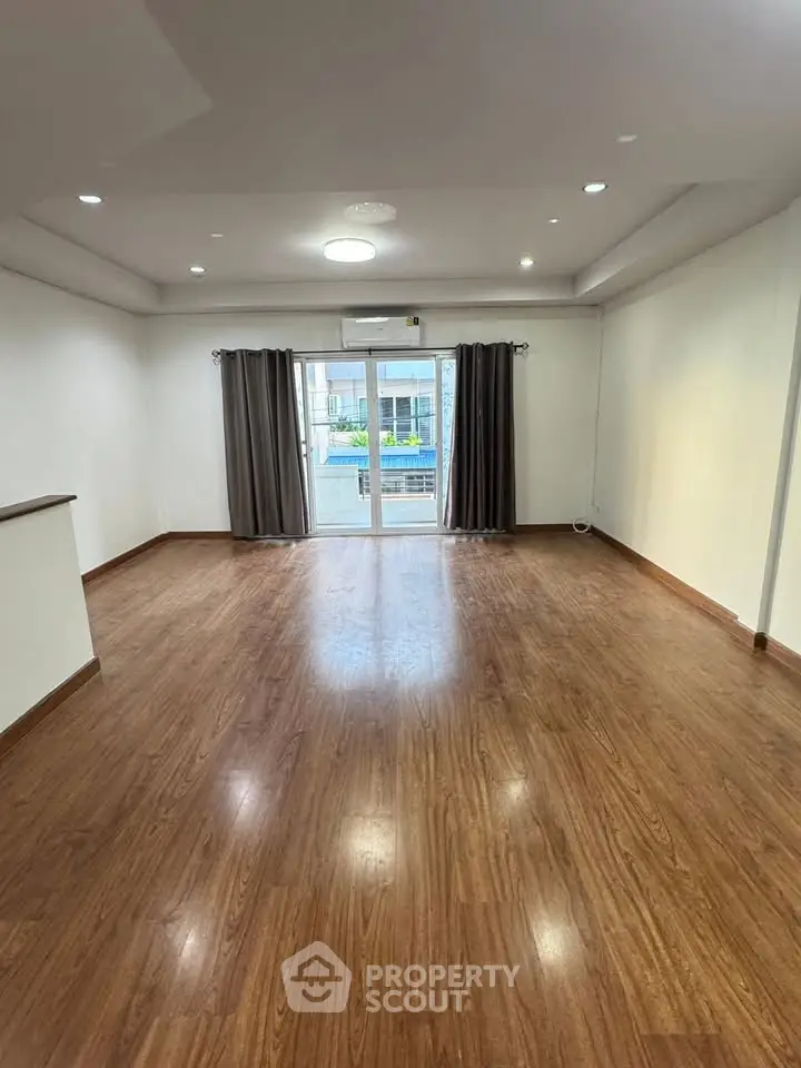 Spacious living room with wooden flooring and large windows offering natural light.