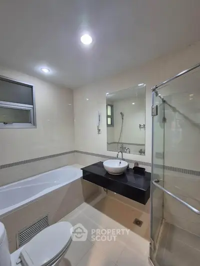 Modern bathroom with bathtub and glass shower enclosure in a sleek, minimalist design.