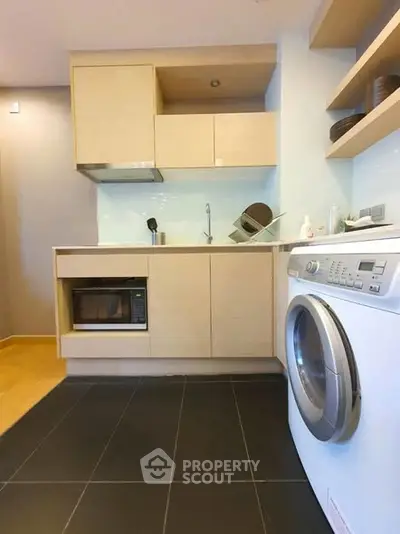 Modern compact kitchen with washing machine and microwave in stylish apartment.