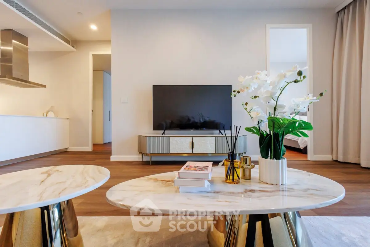 Modern living room with elegant decor and open kitchen layout, featuring a sleek TV setup and stylish furniture.