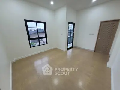 Spacious empty room with wooden flooring and large windows, perfect for customization.