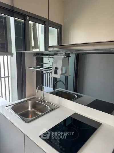 Modern kitchen with sleek induction cooktop and stainless steel sink, featuring large windows for natural light.