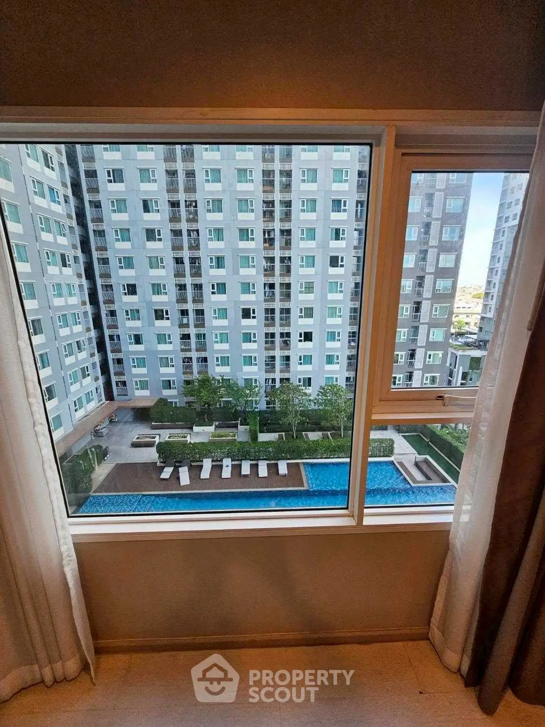 Stunning high-rise apartment view with pool and garden from window, perfect for urban living.
