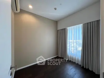Spacious bedroom with large window and elegant curtains, featuring dark wood flooring and neutral wall tones.