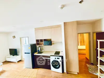 Modern apartment interior with kitchen and living area featuring washing machine and TV.