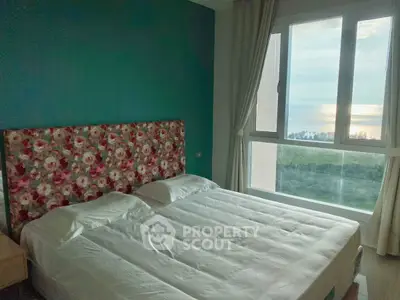 Cozy bedroom with floral headboard and stunning ocean view from large window.