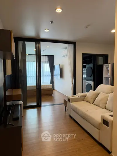 Modern living room with open view to bedroom, featuring sleek furniture and wooden flooring.