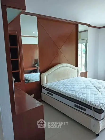 Spacious bedroom with elegant wooden accents and large mirror, featuring a comfortable bed and ample natural light.