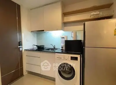 Modern compact kitchen with washing machine and fridge in sleek apartment.