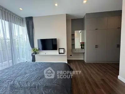 Modern bedroom with large windows and stylish decor, featuring a wall-mounted TV and spacious wardrobe.
