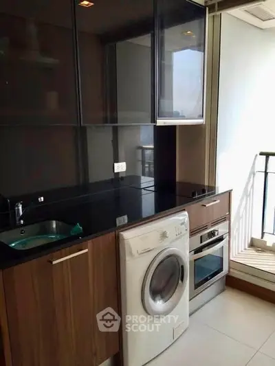 Modern kitchen with sleek cabinets, washing machine, and oven, adjacent to a balcony with natural light.