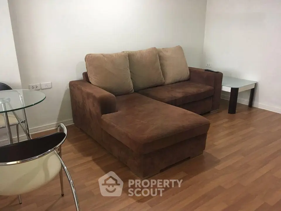 Cozy living room with brown sectional sofa and modern glass table on wooden floor.