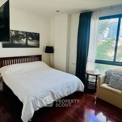 Spacious bedroom with large window and modern decor in urban apartment.
