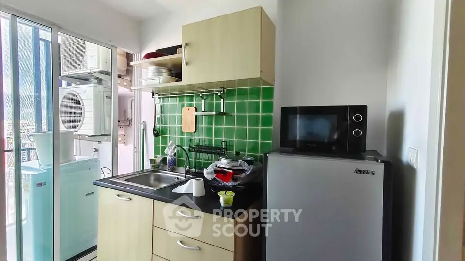 Compact kitchen with green tile backsplash and modern appliances in a cozy apartment.