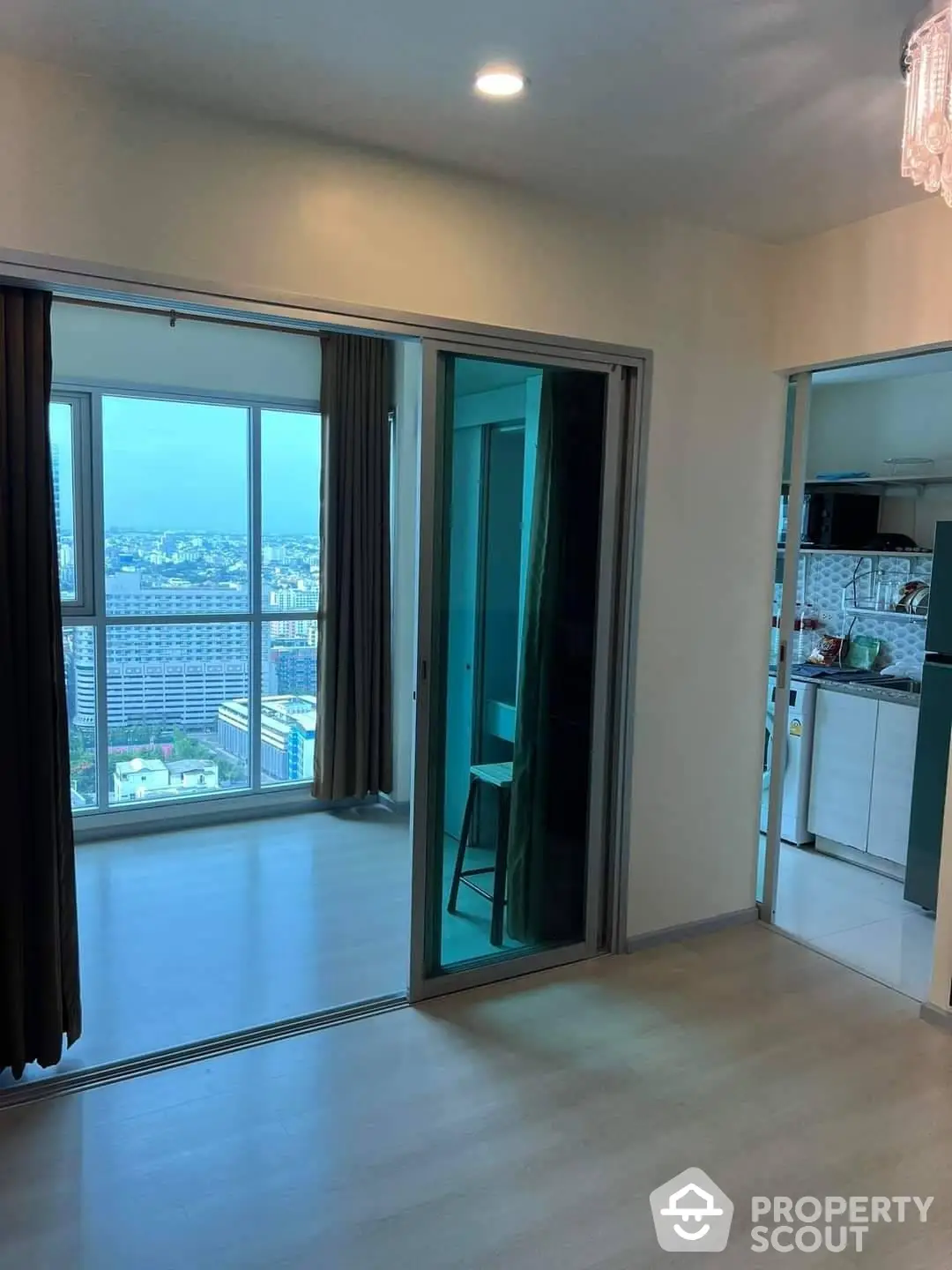 Spacious high-rise apartment with panoramic city views, featuring large windows, modern lighting, and an open layout leading to a cozy balcony.