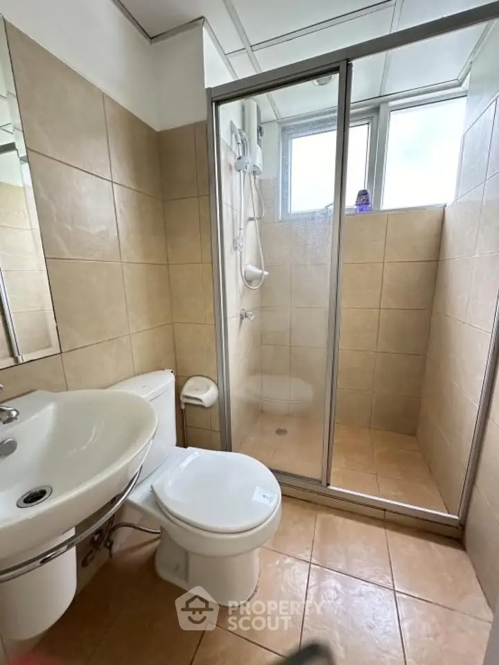 Modern bathroom with tiled walls, glass shower enclosure, and white fixtures.