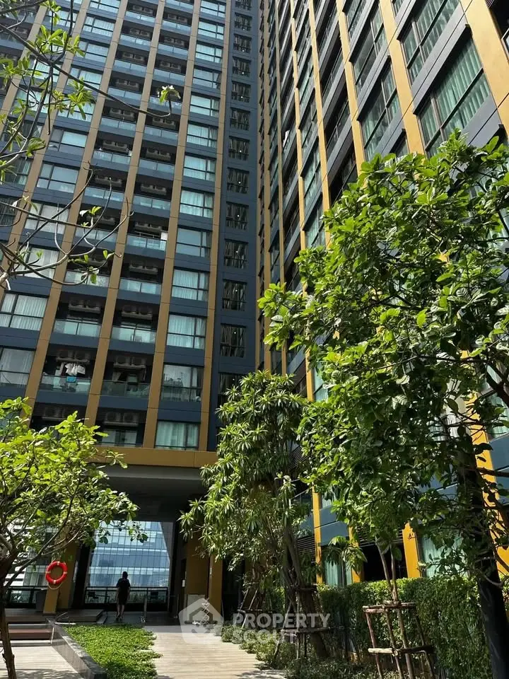 Modern high-rise building with lush garden and tall trees in urban setting.