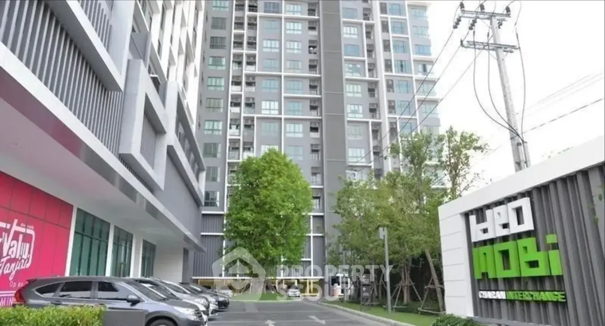 Modern high-rise building with parking and lush greenery at entrance.