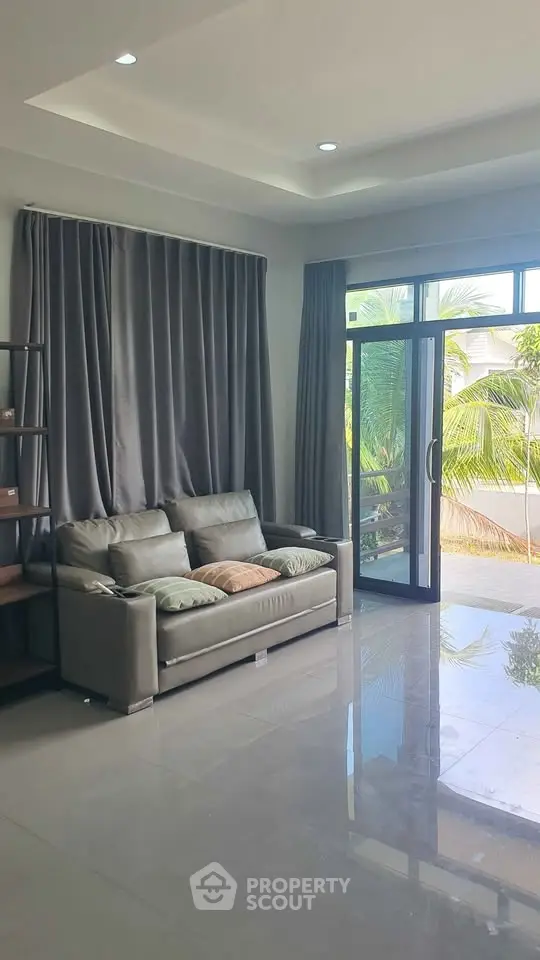 Spacious living room with modern sofa and large windows opening to lush greenery.