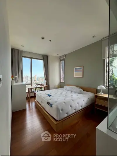 Spacious bedroom with large window offering stunning city views and elegant wooden flooring.