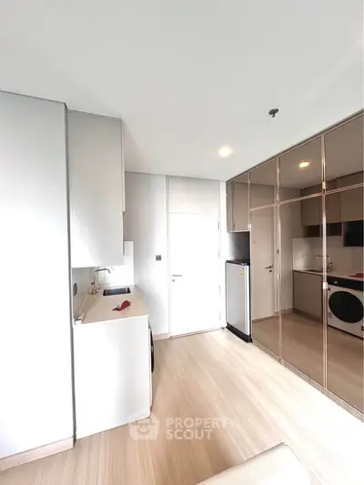 Modern kitchen with sleek cabinetry and mirrored storage, featuring a compact washing machine and refrigerator.