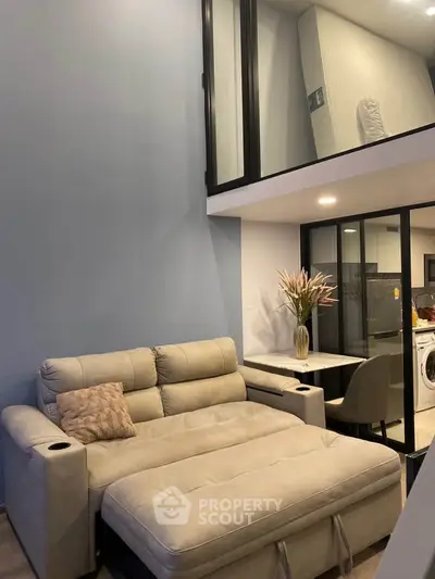 Modern loft-style living room with cozy beige sofa and sleek glass railing, featuring a compact workspace and washing machine.