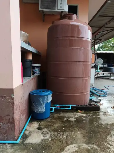 Large outdoor water tank beside a building with plumbing connections