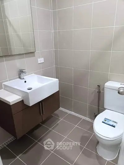Modern bathroom with sleek sink and toilet in a tiled setting.