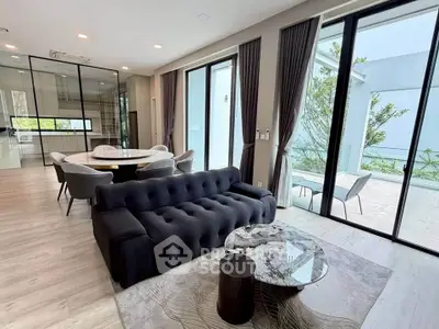 Modern living room with sleek black sofa, glass doors opening to a spacious balcony, and elegant dining area.