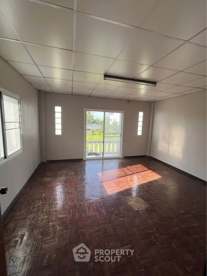Spacious empty room with parquet flooring and large windows for natural light.