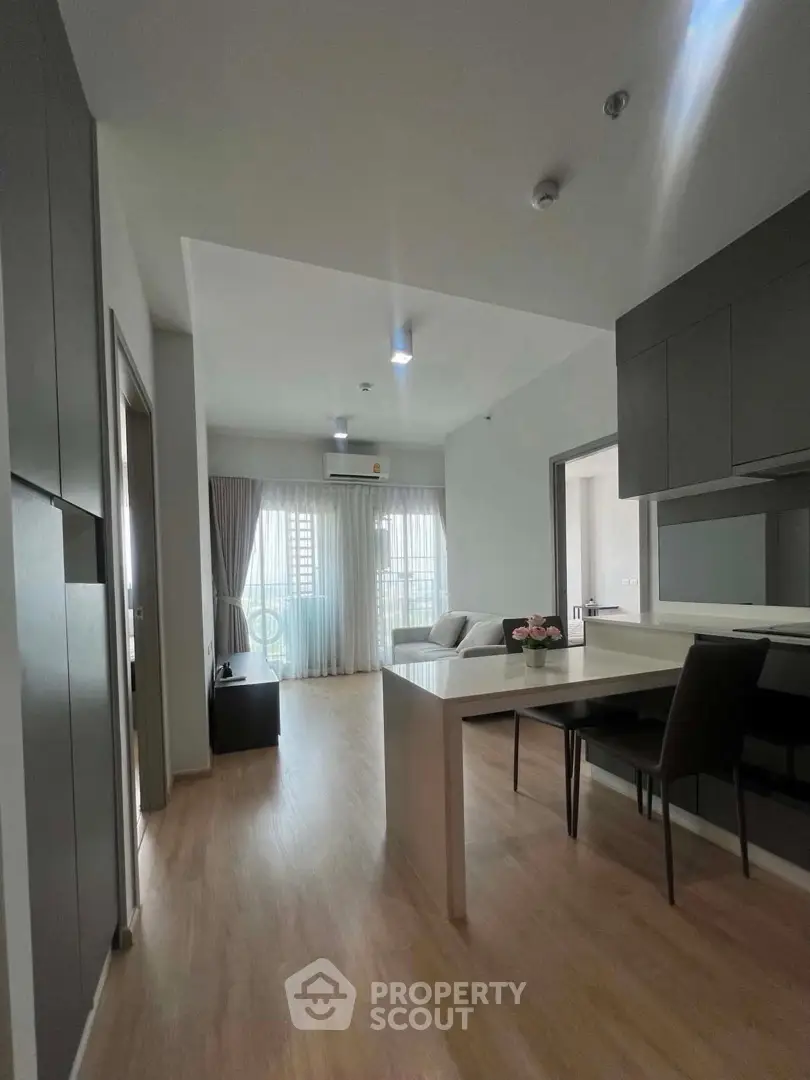 Modern open-plan living room with sleek kitchen and dining area, featuring natural light and contemporary design.