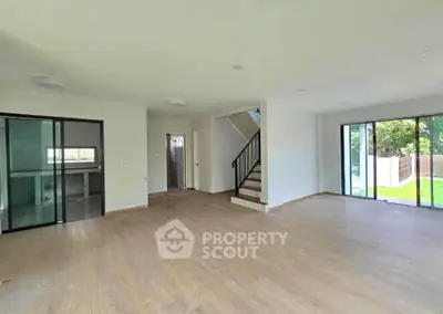 Spacious modern living room with large windows and garden view, featuring sleek staircase and open layout.