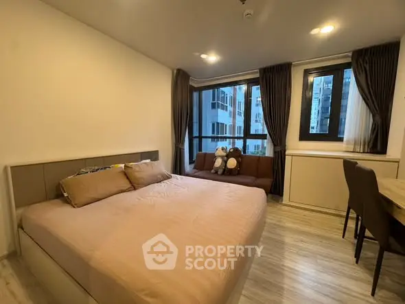 Modern bedroom with large windows and cozy seating area in urban apartment.