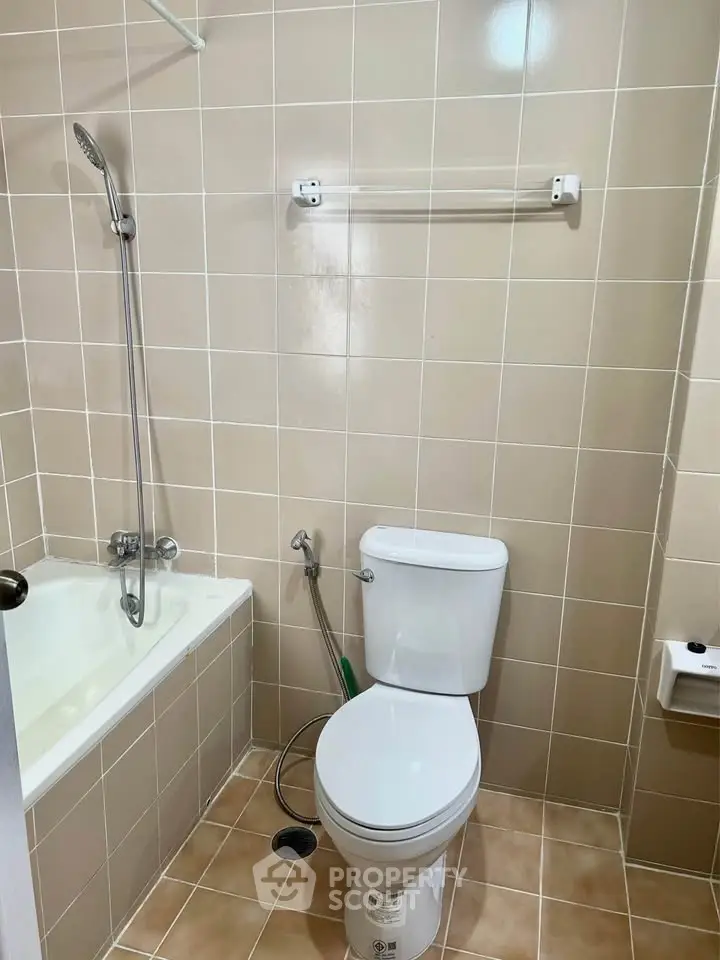 Modern bathroom with beige tiles, bathtub, and toilet in a compact layout.
