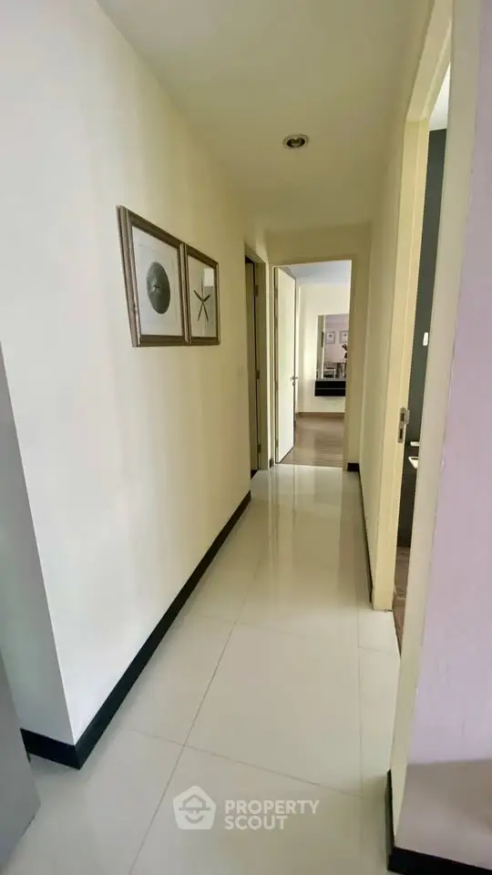 Bright hallway with polished floors leading to a cozy bedroom, featuring modern wall art and sleek design.