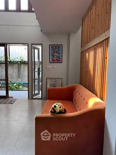 Stylish living room with orange sofa and modern decor, featuring natural light and wooden accents.