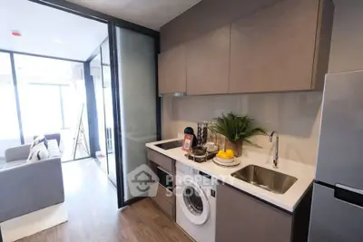 Modern kitchen with sleek cabinetry, washing machine, and open layout leading to a bright living area.
