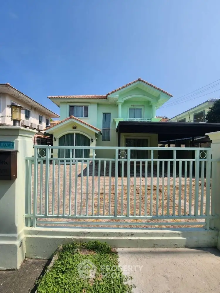Charming two-story mint green house with gated driveway and tiled roof.