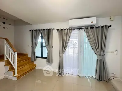 Modern living room with staircase and large windows, featuring elegant curtains and air conditioning.