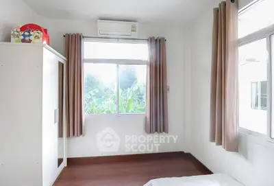 Bright bedroom with large window and air conditioning, featuring wooden floors and neutral curtains.
