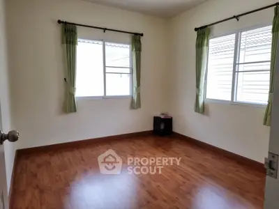 Spacious empty room with wooden flooring and large windows, perfect for customization.