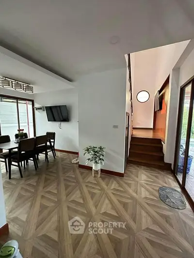 Spacious modern living area with stylish flooring and natural light, featuring a dining set and wall-mounted TV.