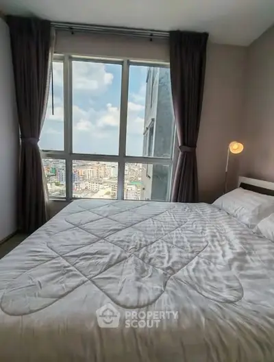 Spacious bedroom with large window offering stunning city view, perfect for urban living.