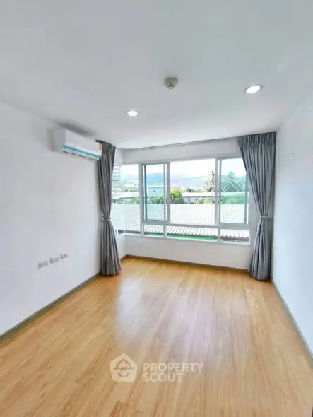Bright empty room with large windows and wooden flooring, perfect for customization.