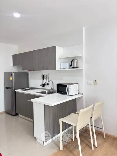 Modern kitchen with sleek cabinetry, compact appliances, and breakfast bar seating in a stylish apartment.