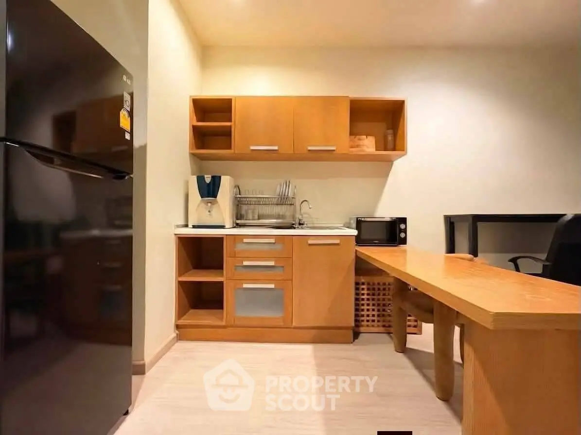 Modern compact kitchen with wooden cabinets and sleek appliances in cozy apartment.