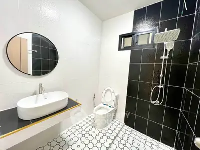 Modern bathroom with stylish black and white tiles, round mirror, and sleek fixtures.